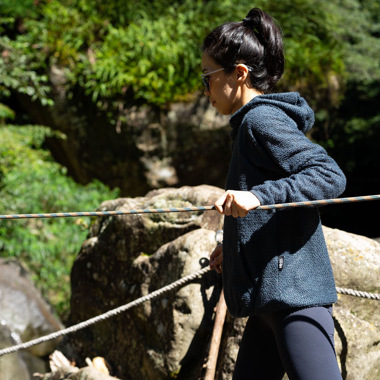 A female hiker modeling ultralight mid layer and leggings while walking across a rocky stream crossing